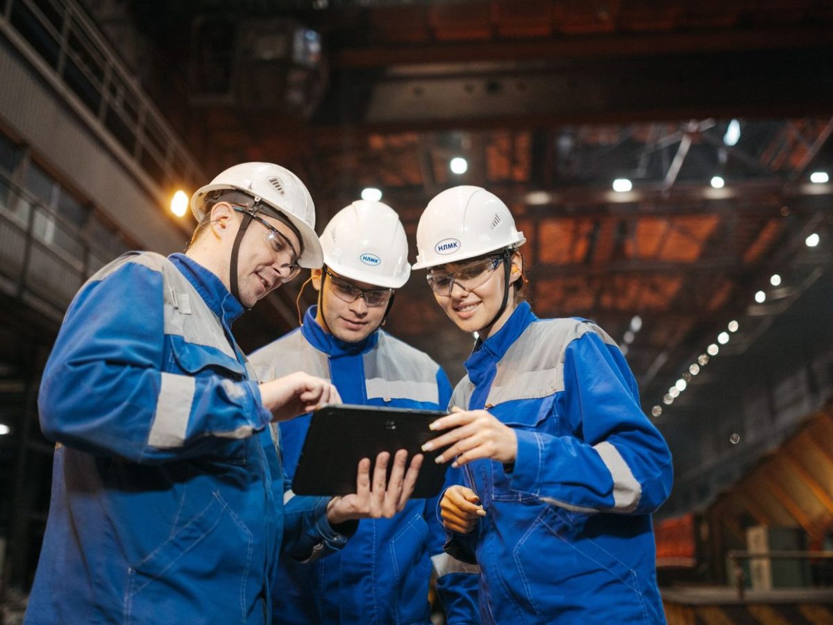 Tres tecnicos industriais de capacete colaborando diante de um tablet
